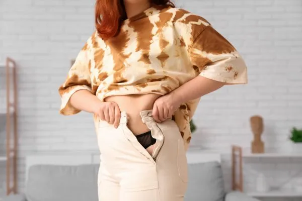 Image of woman trying to do her trousers up after pregnancy weight gain Coombe