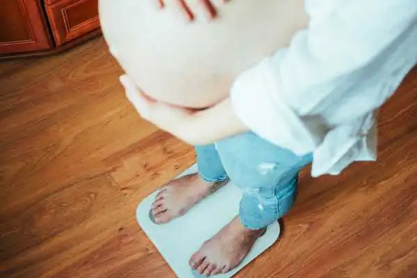 Image of woman weighing herself and experiencing weight gain through pregnancy Coombe